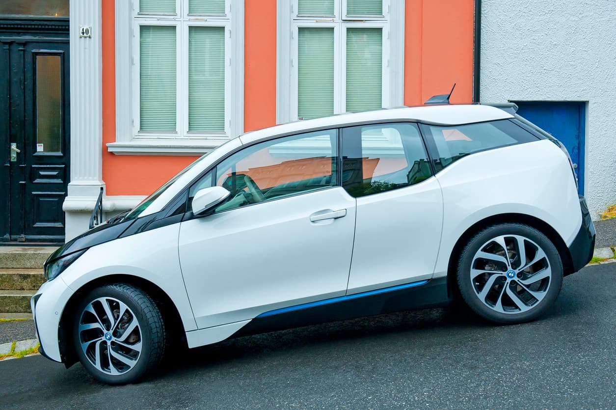 Hvit elbil parkert ved fargerik husfasade i bygate, brukt som illustrasjon i artikkel om bil solgt som den er.