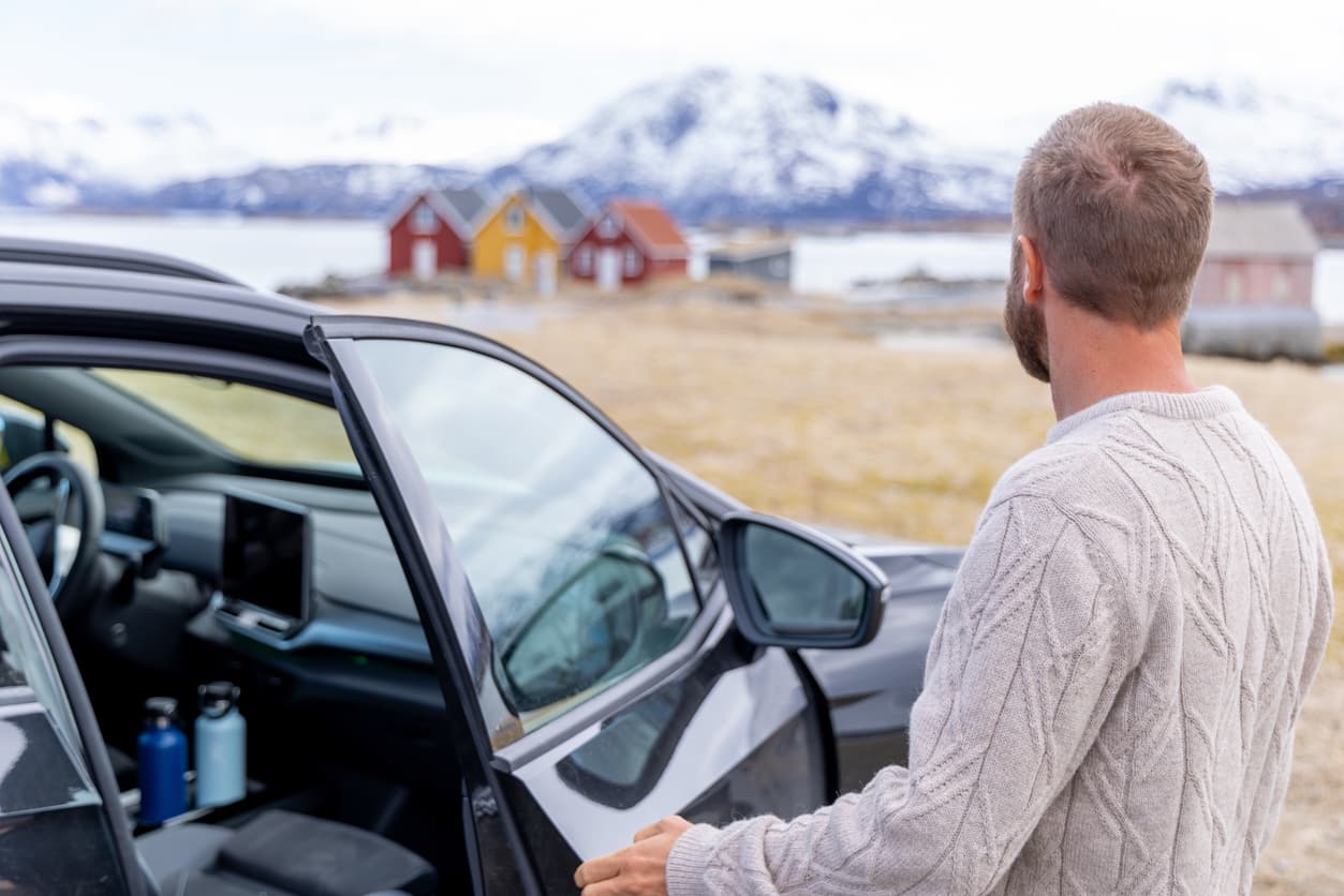 Mann åpner døra på en mørk SUV foran fjord og snødekte fjell, illustrasjon til artikkel om frister hvis du har kjøpt bruktbil med feil.