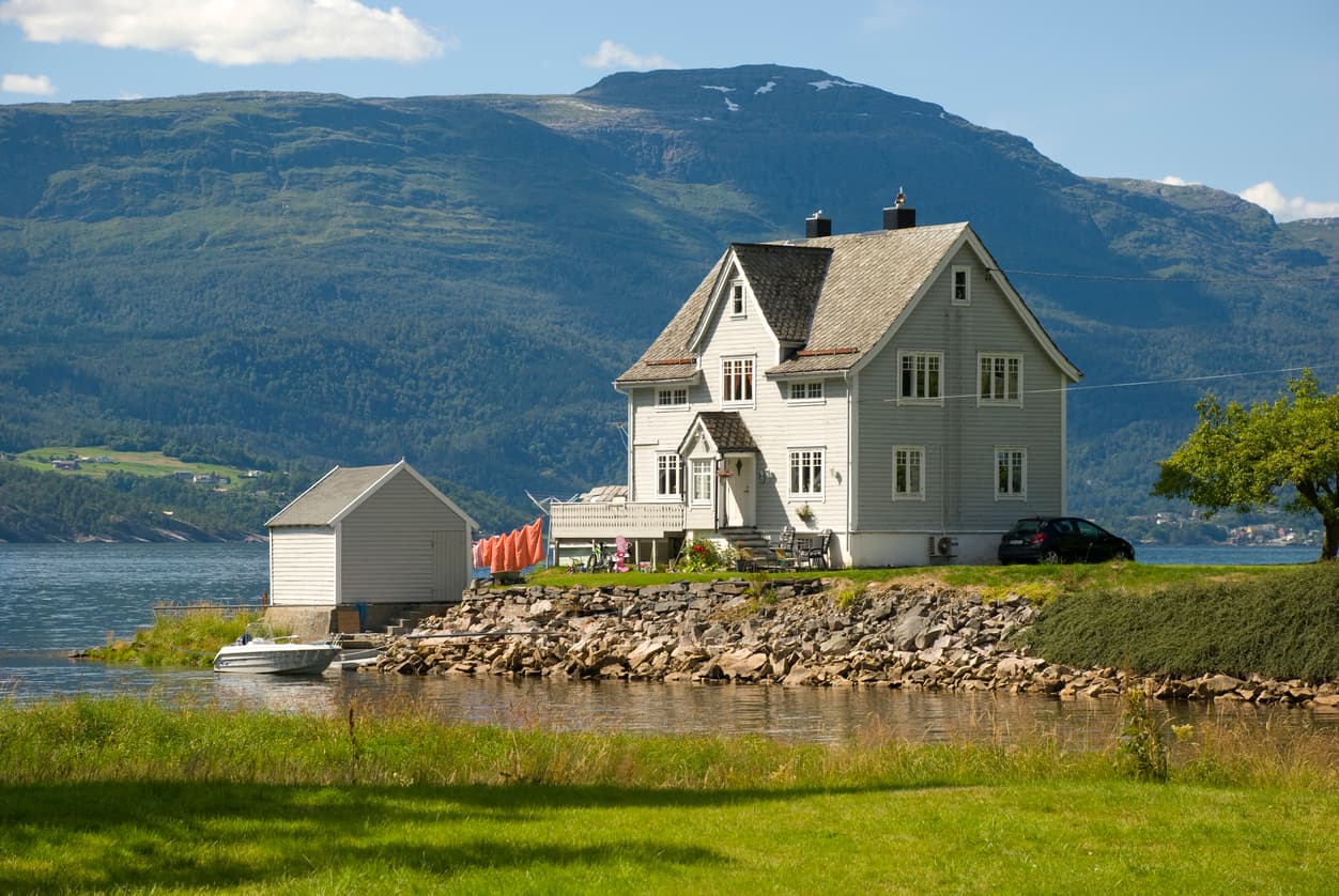 Hvitt sveitserhus ved fjorden med fjellandskap i bakgrunnen, brukt som illustrasjon i artikkel om å angre på boligkjøp.