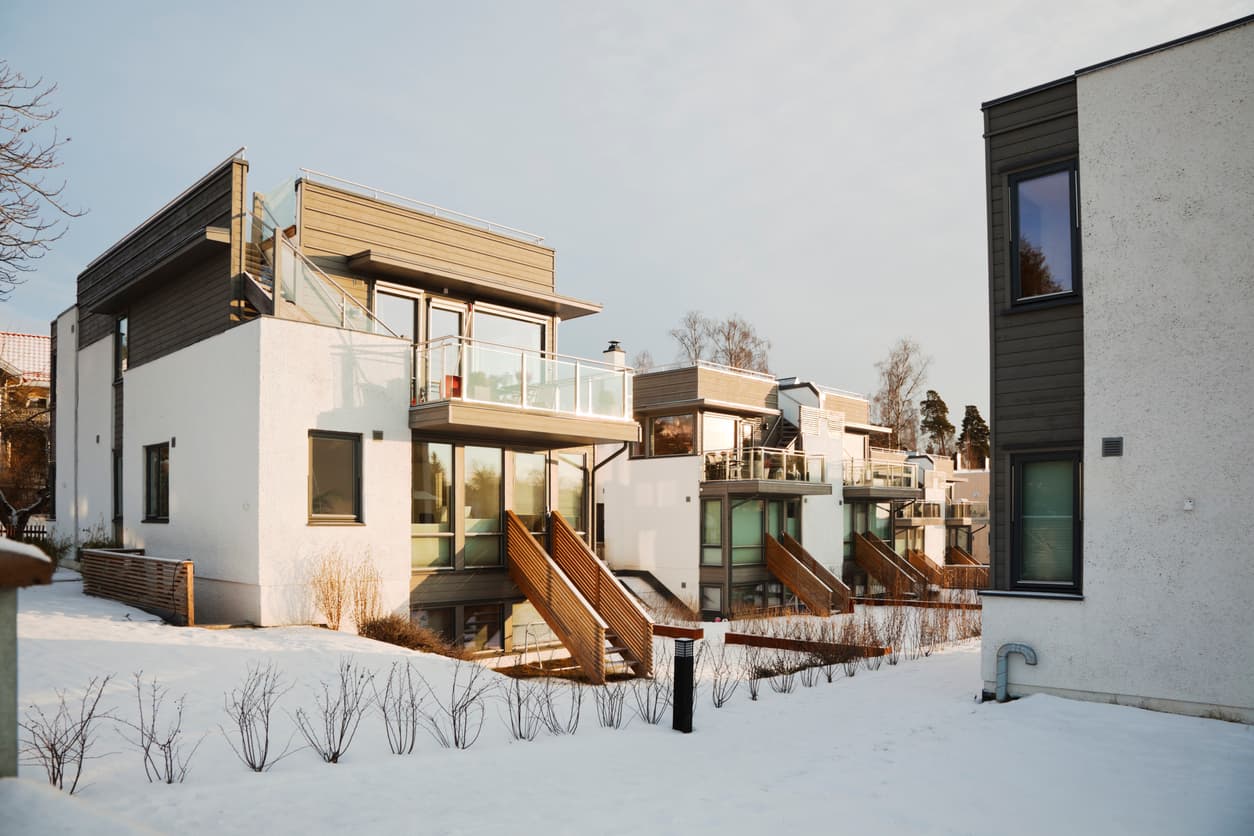 Moderne rekkehus i hvit puss og mørkt treverk med glassrekkverk og snødekt bakke, brukt som illustrasjon i artikkel om garanti ved kjøp av nybygg.