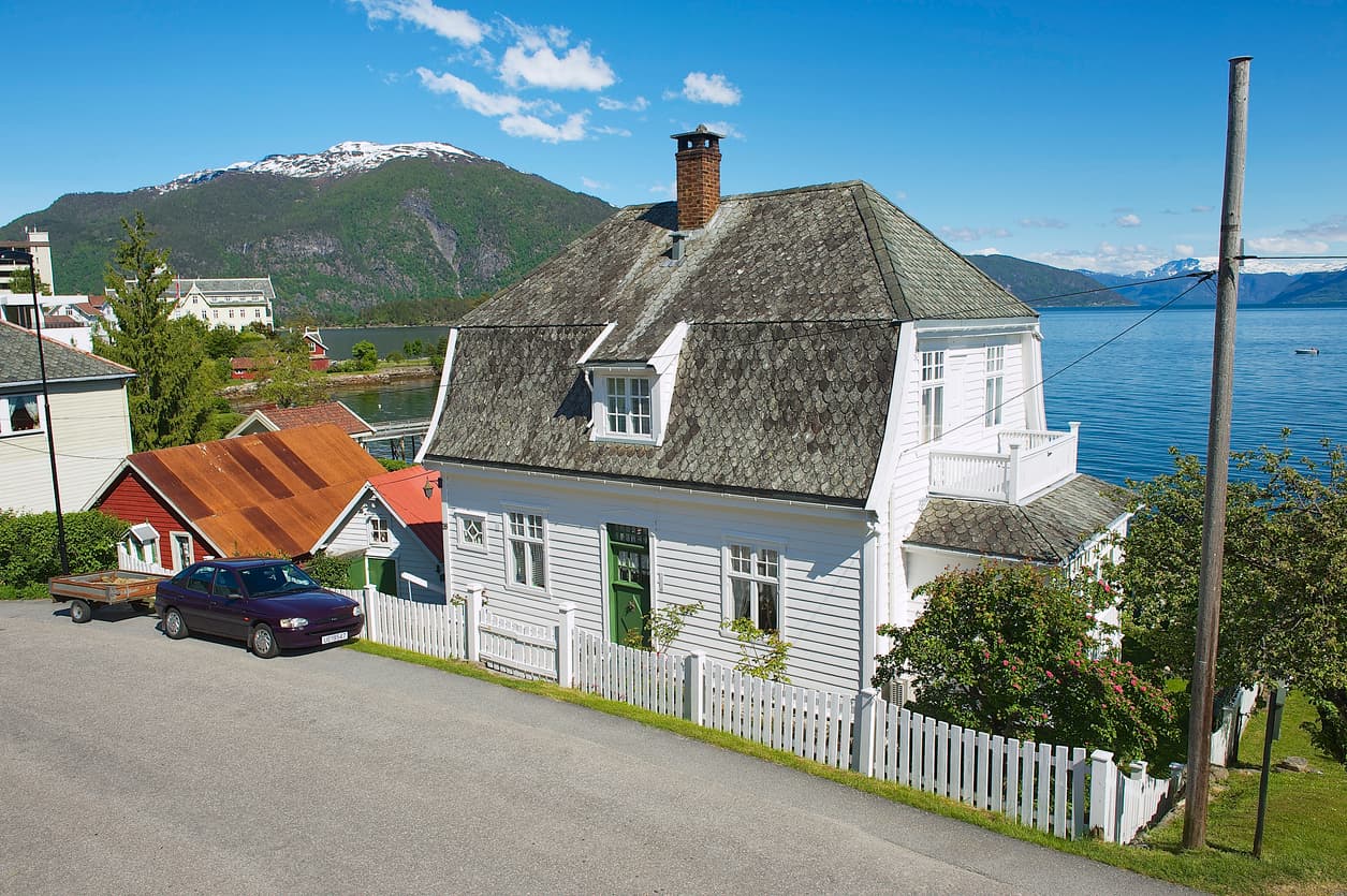 Hvitt trehus ved fjorden med snøkledde fjell i bakgrunnen, brukt som illustrasjon i artikkel om frist for å klage på boligkjøp.