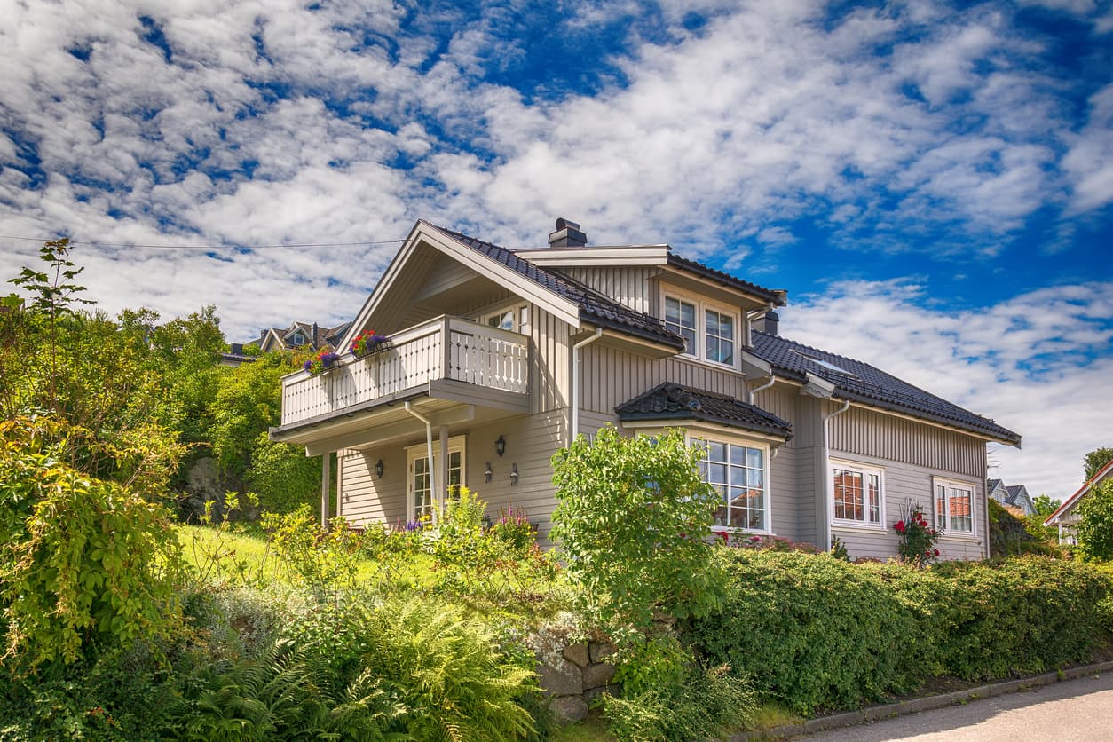 Grått norsk trehus med balkong og frodig hage under skyet himmel, brukt som illustrasjon i artikkel om bolig uten papirer på ferdig arbeid.