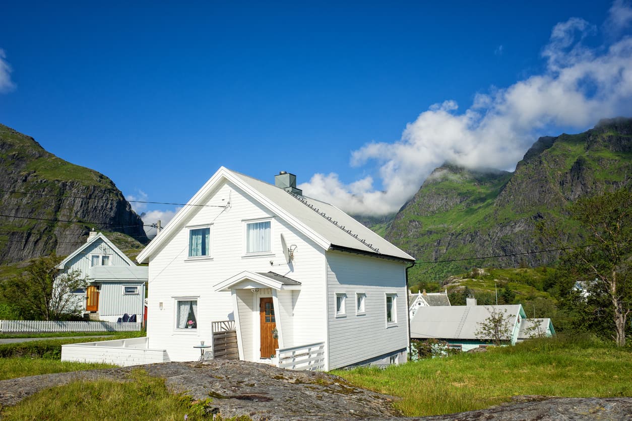 Hvit trebolig i typisk norsk landskap med fjell i bakgrunnen, brukt som illustrasjon i artikkel om prisavslag ved boligkjøp.