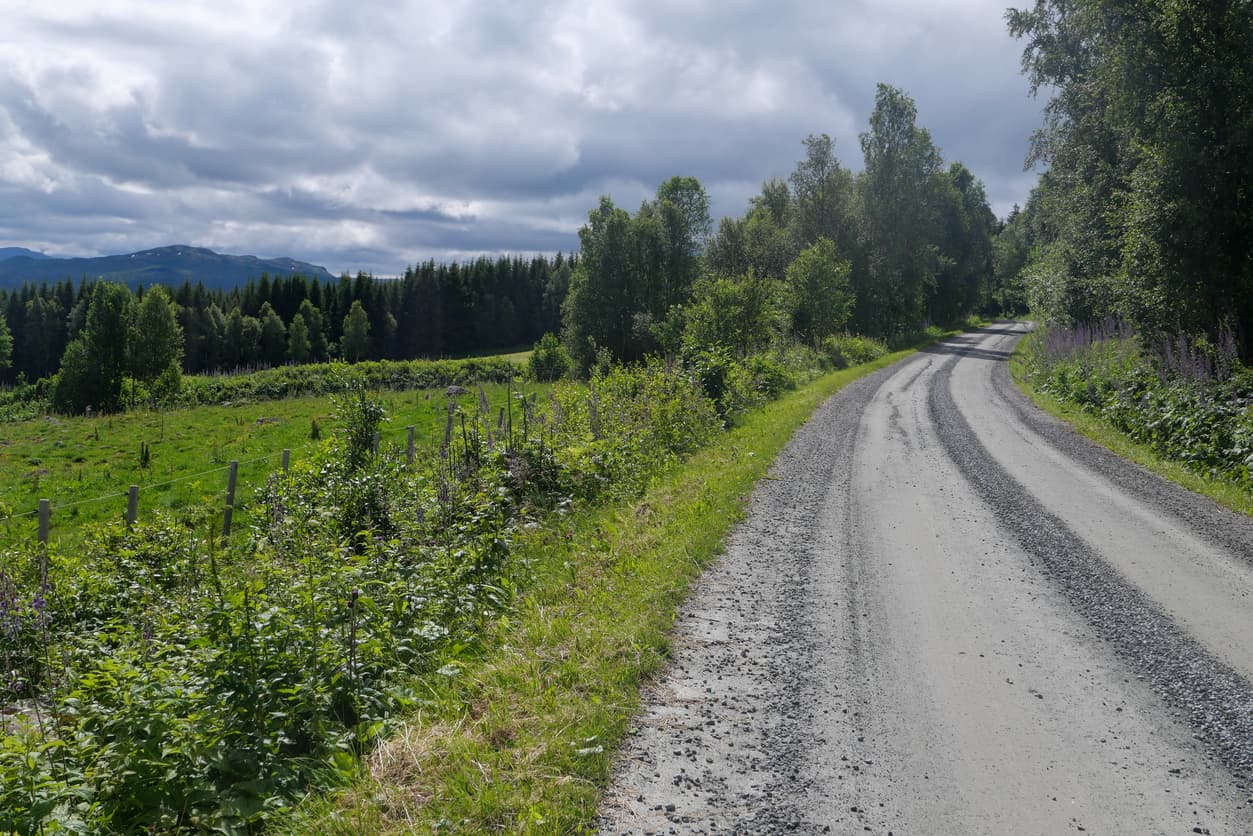 Smal grusvei gjennom jordbrukslandskap med gjerde og fjell i bakgrunnen, brukt i artikkel om rett til vei og rettssak.