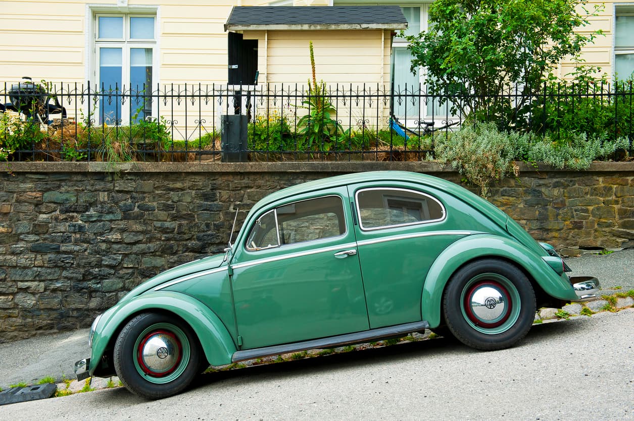 Lysegrønn veteranbil av typen Volkswagen Boble står parkert langs steinmur i boliggate, illustrasjon til artikkel om hva bilforsikring dekker.