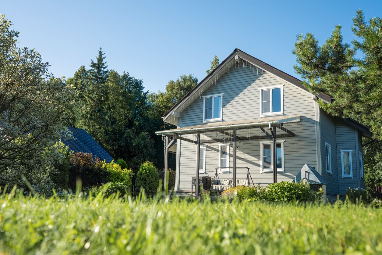Grått trehus med pergola og hagegynge sett fra høy plen, brukt som illustrasjon i artikkel om boligkjøper og reklamasjon.