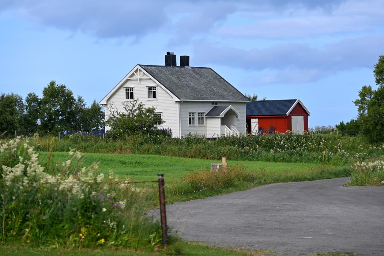 Hvitt våningshus med rød driftsbygning på et gårdstun, brukt som illustrasjon i artikkel om festetomt og gjeldende regler.