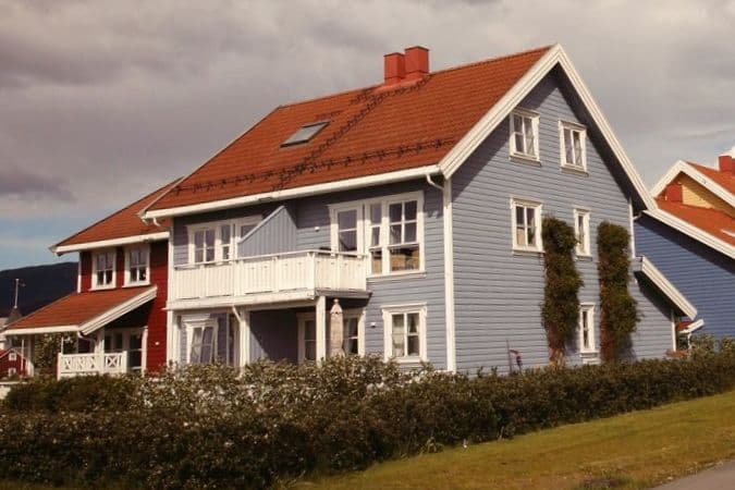 Blått trehus med hvite vinduer, rødt teglsteinstak og veranda bak en hekk, brukt som illustrasjon i artikkel om samlivsbrudd og felles bolig.