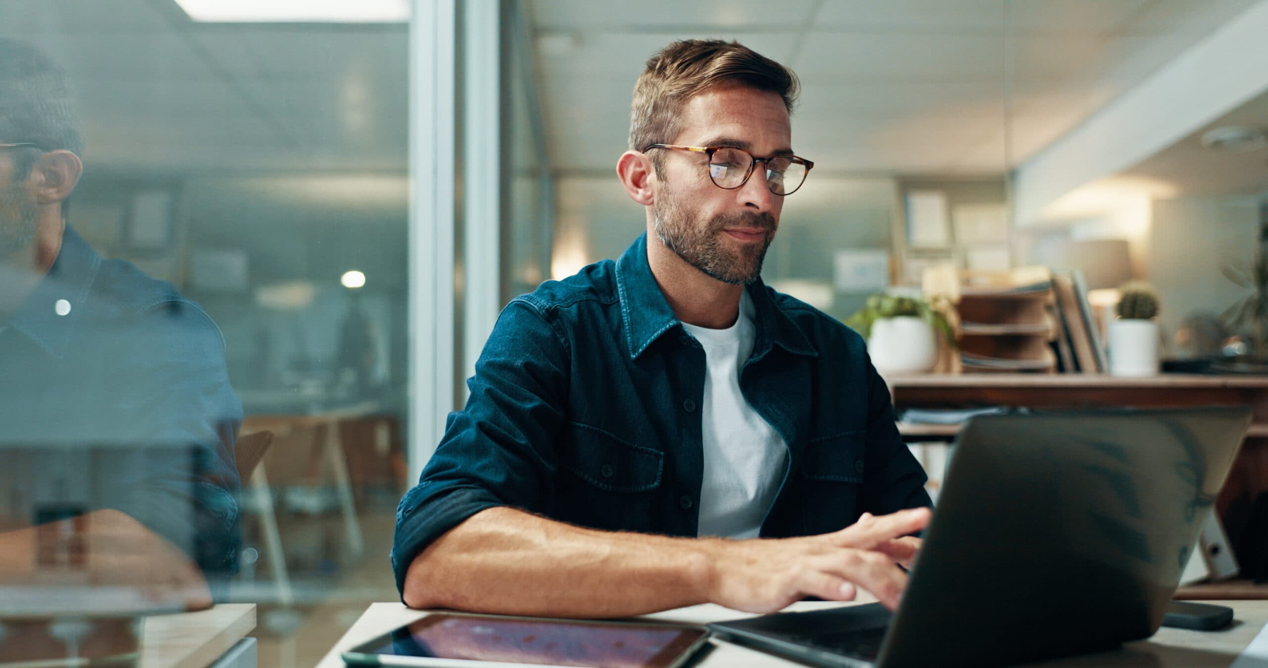 Mann med briller jobber konsentrert på laptop ved et skrivebord på kontoret, illustrasjon til artikkel om at arbeidsgiver bestrider sykemelding.