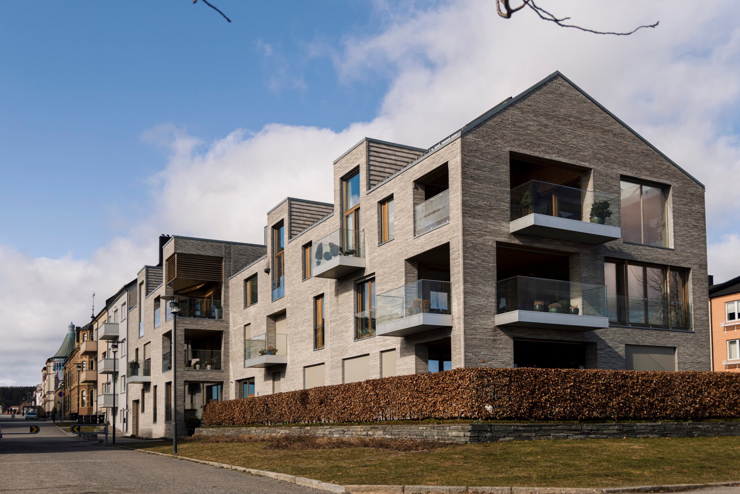 Nyoppført boligblokk i grå tegl med glassrekkverk på balkongene og bøkehekk i forkant, brukt som illustrasjon i artikkel om klage etter lovverket.