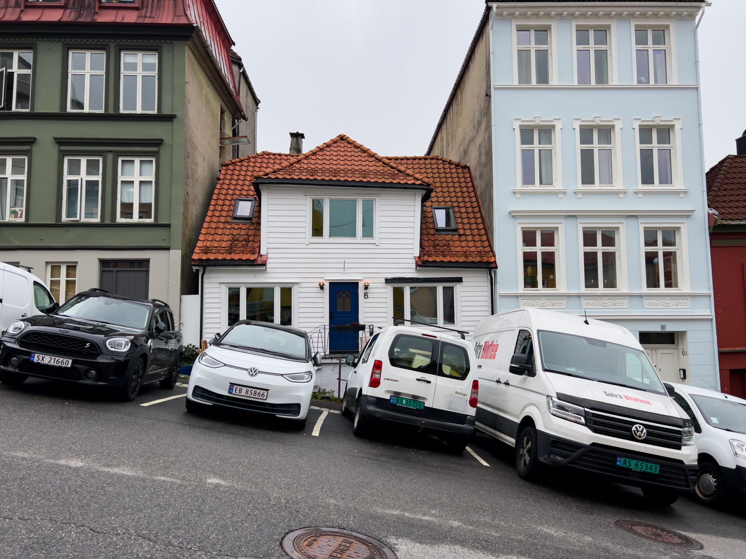 Tett parkerte biler på oppmerkede plasser i en bratt bygate i Bergen, brukt som illustrasjon i artikkel om bredde på en p-plass.