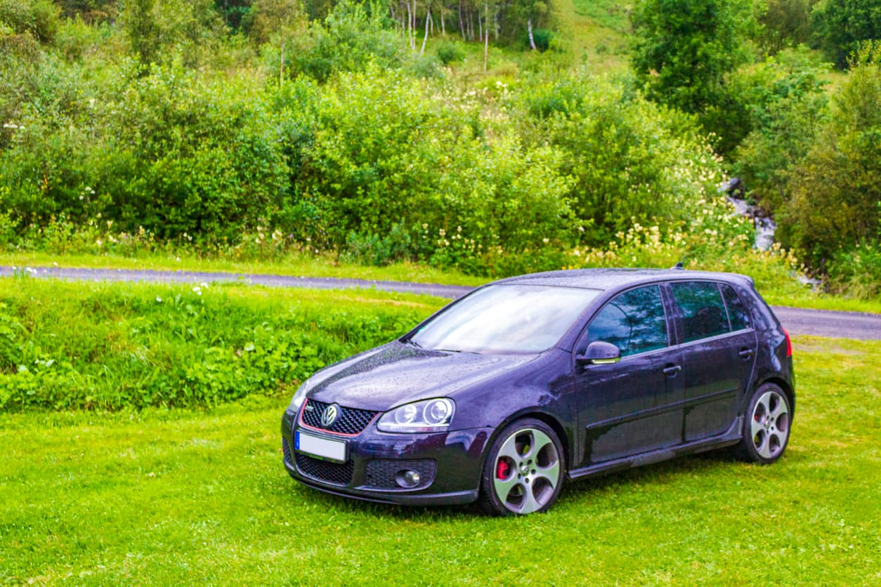 Mørk VW Golf GTI parkert på gress ved en grusvei og grønn skog, brukt som illustrasjon i artikkel om ansvar ved privat salg av bil.