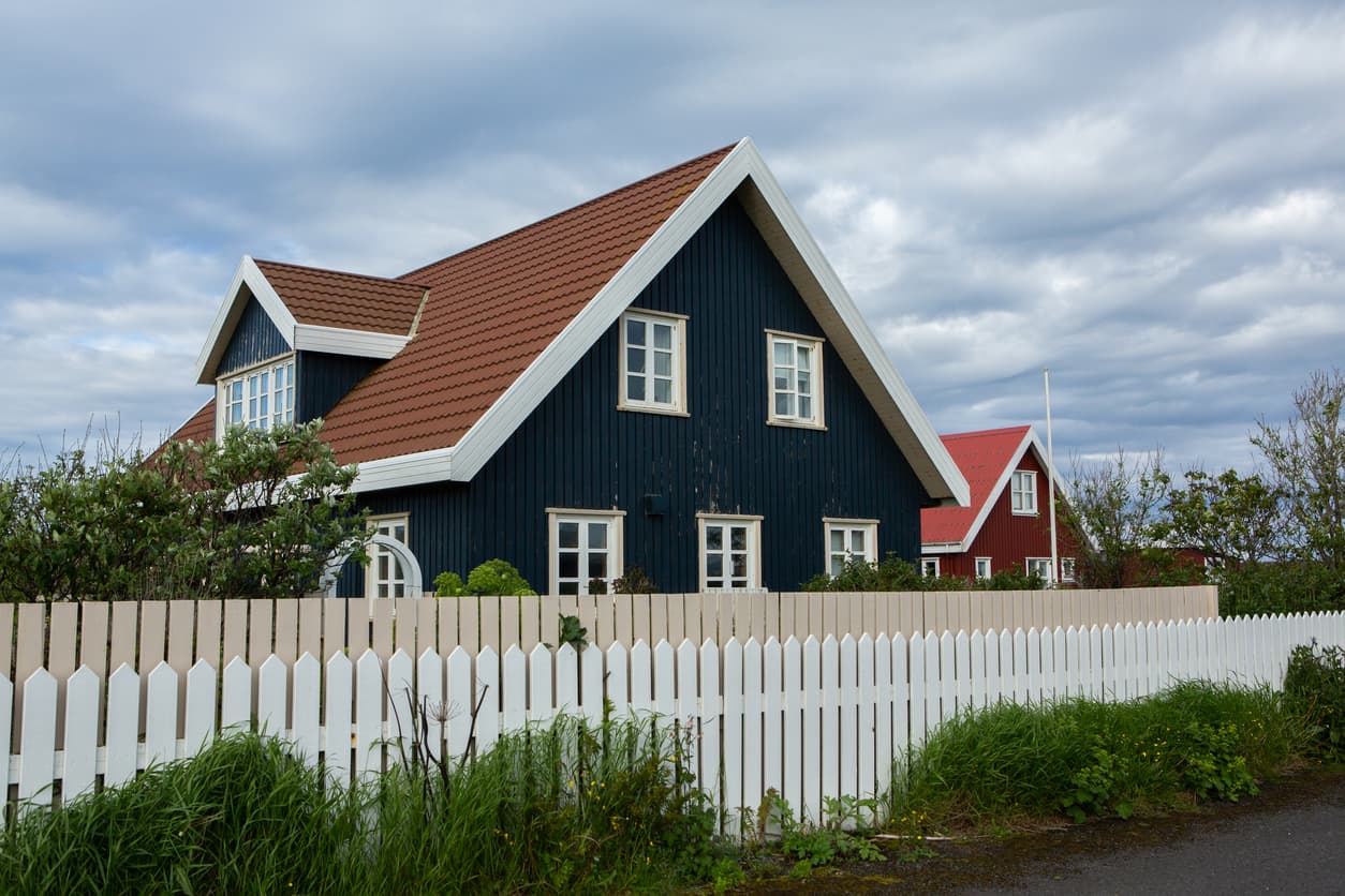 Mørkeblått norsk trehus med rødt tegltak og hvitt stakittgjerde, brukt som illustrasjon i artikkel om avhendingsloven § 3-4.