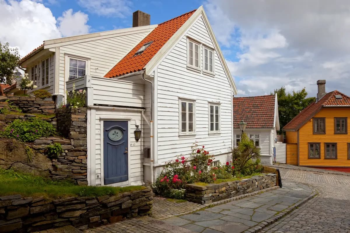 Sjarmerende hvitt trehus med oransje tak og blå dør i en tradisjonell norsk gate.