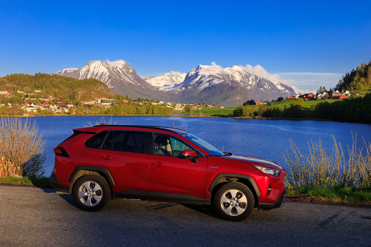 Rød Toyota RAV4 parkert ved en fjord med snødekte fjell i bakgrunnen, brukt som illustrasjon i artikkel om bilkjøp ved fjernsalg.