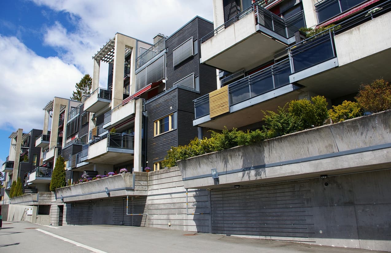 Moderne leilighetskompleks i mørk trekledning og betong med balkonger og garasjeanlegg, brukt som illustrasjon i artikkel om felleskostnader i et sameie.