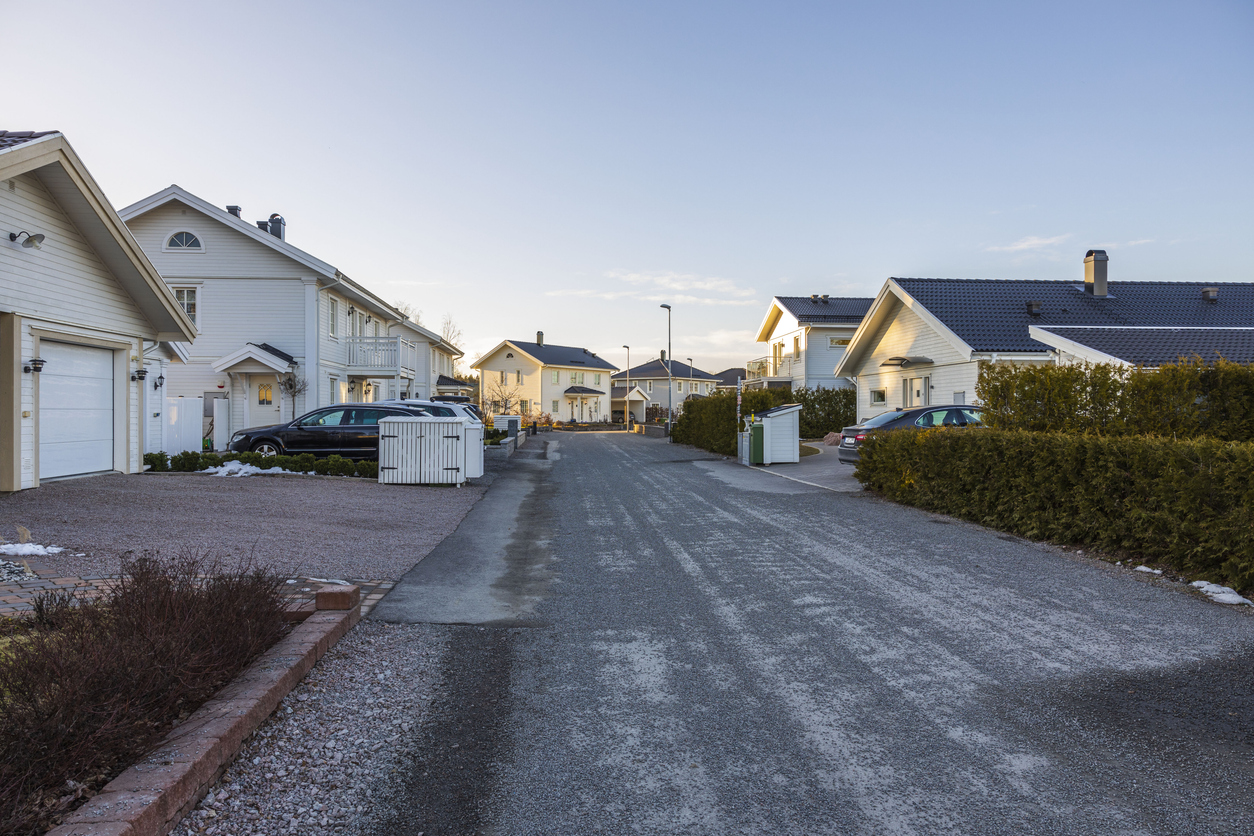 Frostdekket grus- og asfaltdekke gjennom et boligfelt med hvite trehus, brukt som illustrasjon i artikkel om regler for privat vei.