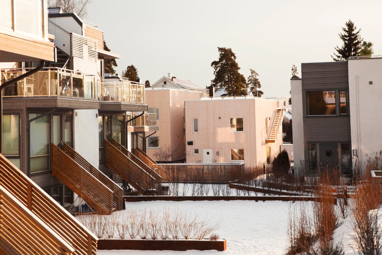 Moderne rekkehus i tre og lys puss med snødekt fellesareal og brede utvendige trapper, brukt som illustrasjon i artikkel om vedtektsendringer i sameie.