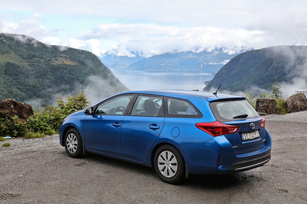 Blå Toyota stasjonsvogn med norske skilter parkert på grusplass over en fjord, brukt som illustrasjon i artikkel om kjøp av bruktimportert bil.
