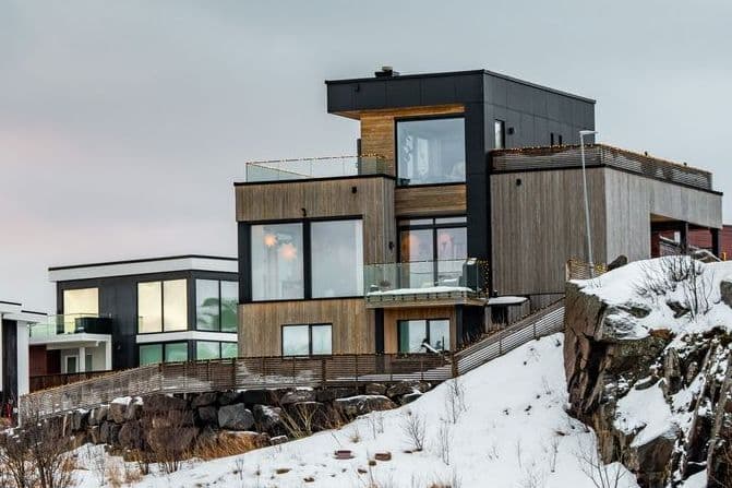 Nyoppførte eneboliger med trekledning og store vinduer på en bergknaus i vinterlandskap, illustrasjon til sak om å heve boligkjøp av nybygg.