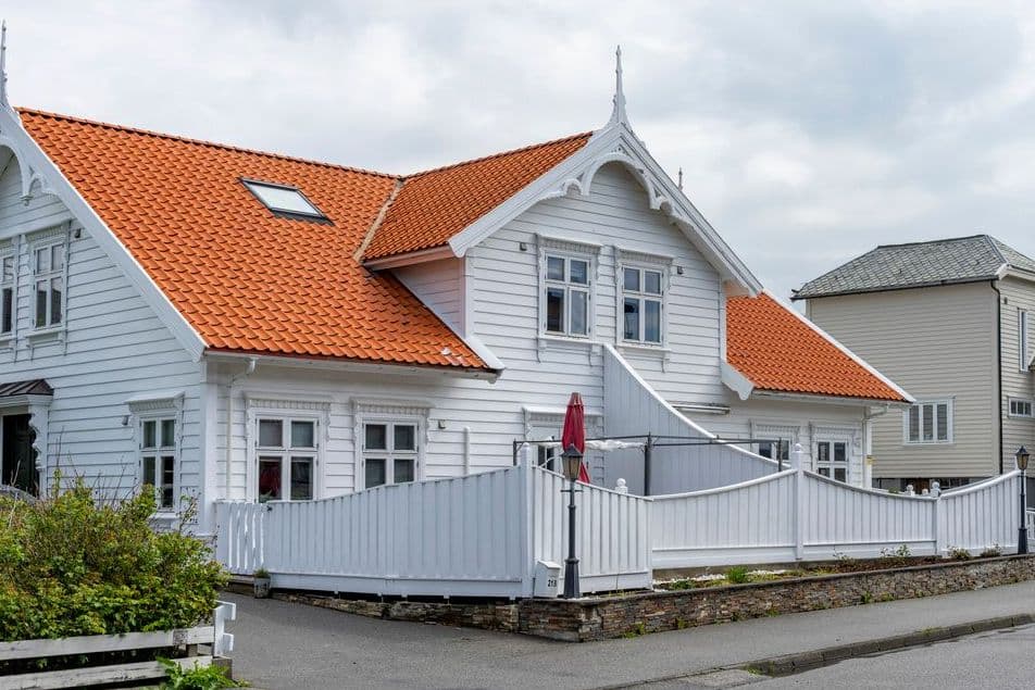 Hvitt trehus i sveitserstil med oransje takstein og hvitt stakitt mot gaten, illustrasjon til sak om hva selger gjør når kjøper trekker seg fra avtale om boligkjøp.